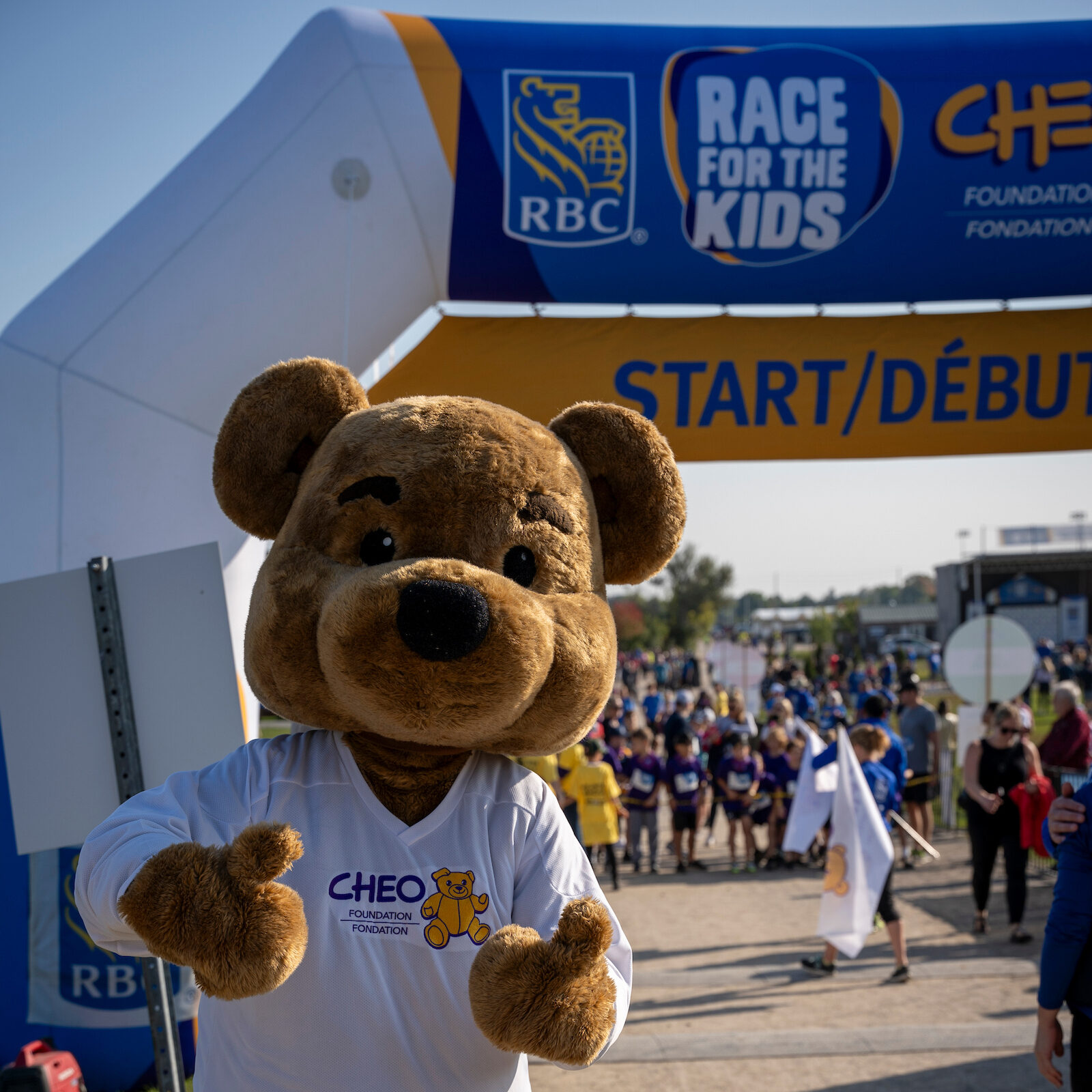 CHEO's mascot, a teddy bear, stands in a CHEO t-shirt at the start line at CHEO's RBC Race for the Kids.